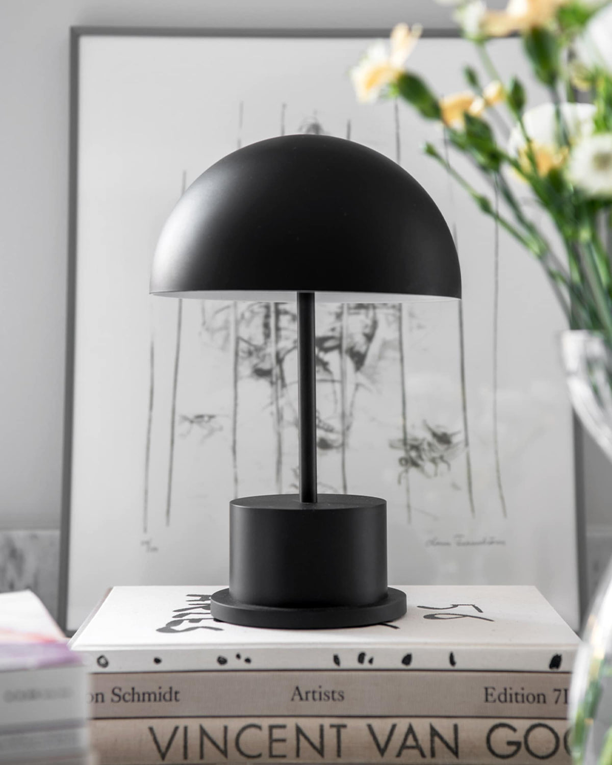 matte black portable lamp styled on bookshelf beside framed artwork
