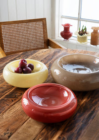 maroon sculptural glass bowl styled on wooden dining table with other colourful bowls
