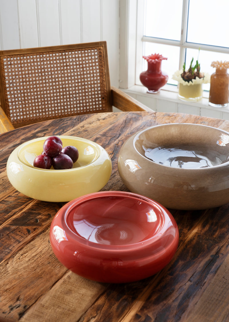 maroon sculptural glass bowl styled on wooden dining table with other colourful bowls
