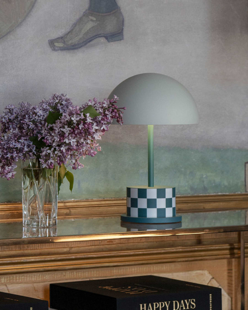 Riviera Checkers portable lamp with teal patterned base on mantel beside lilac flowers
