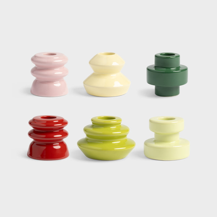 Alt: close-up of assorted &klevering candle holders in red green pink and cream on dark tabletop
