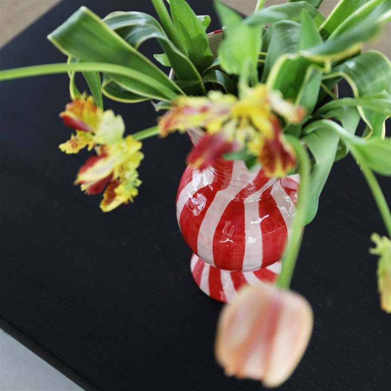 overhead detail of &klevering red striped rhombic vase and tulips on dark table
