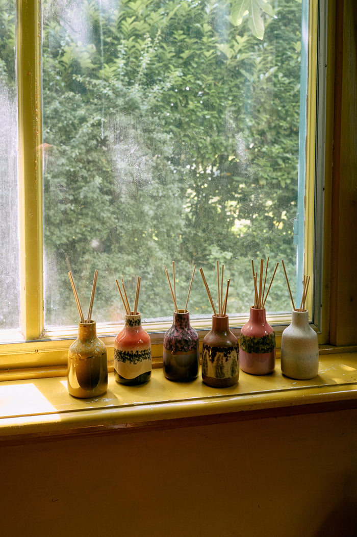Set of HKLIVING diffuser bottles with sticks on a windowsill with a view of greenery outside.