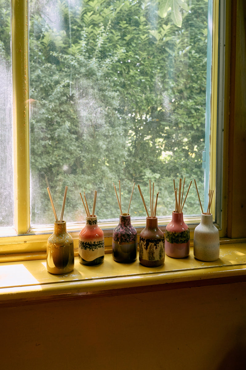 Set of HKLIVING diffuser bottles with sticks on a windowsill with a view of greenery outside.
