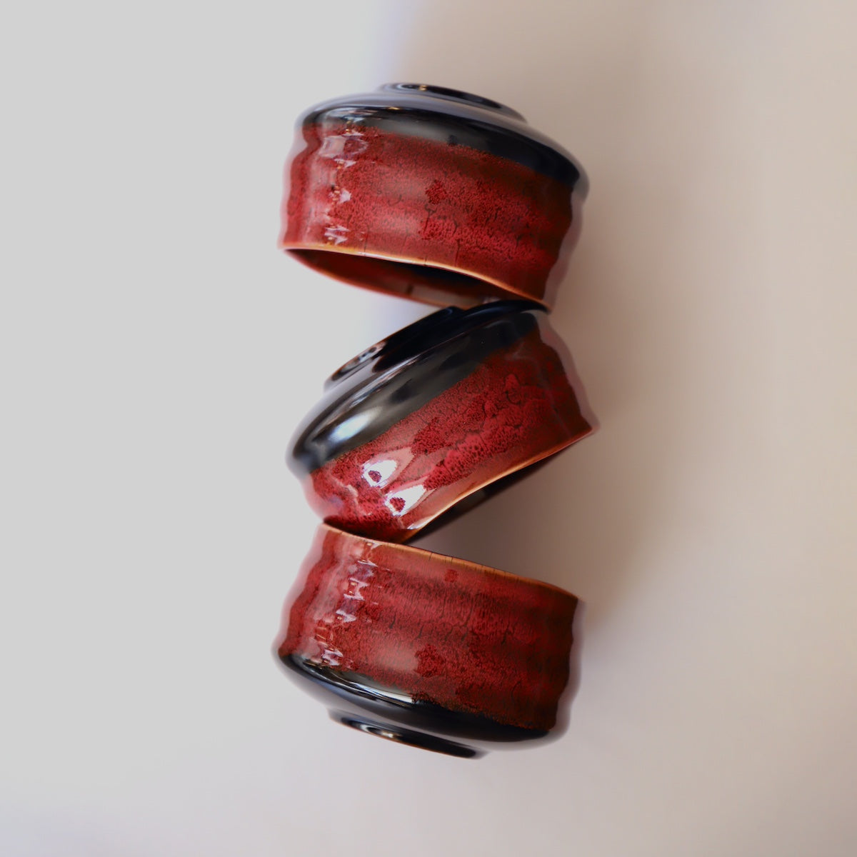 Three stacked red lava ceramic matcha bowls showing glaze variation and finger grooves