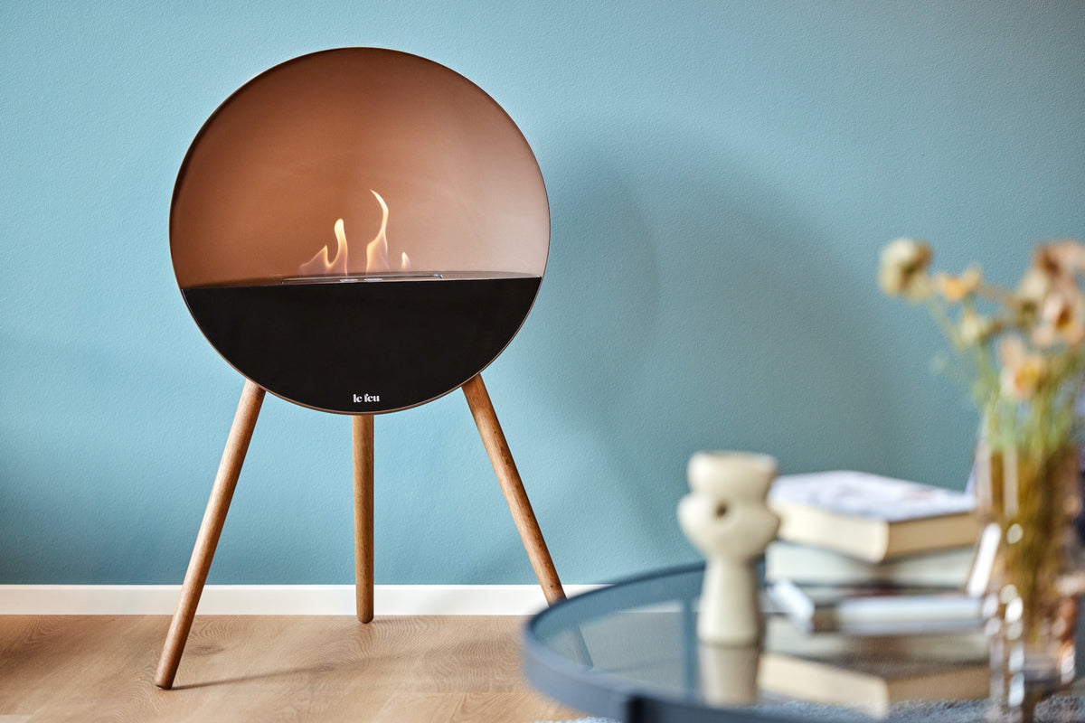 Le Feu Eye bioethanol fireplace with mocca dome and smoked oak legs creating warm Scandinavian atmosphere in a modern living room with blue wall