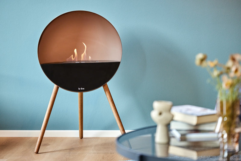 Le Feu Eye bioethanol fireplace with mocca dome and smoked oak legs creating warm Scandinavian atmosphere in a modern living room with blue wall