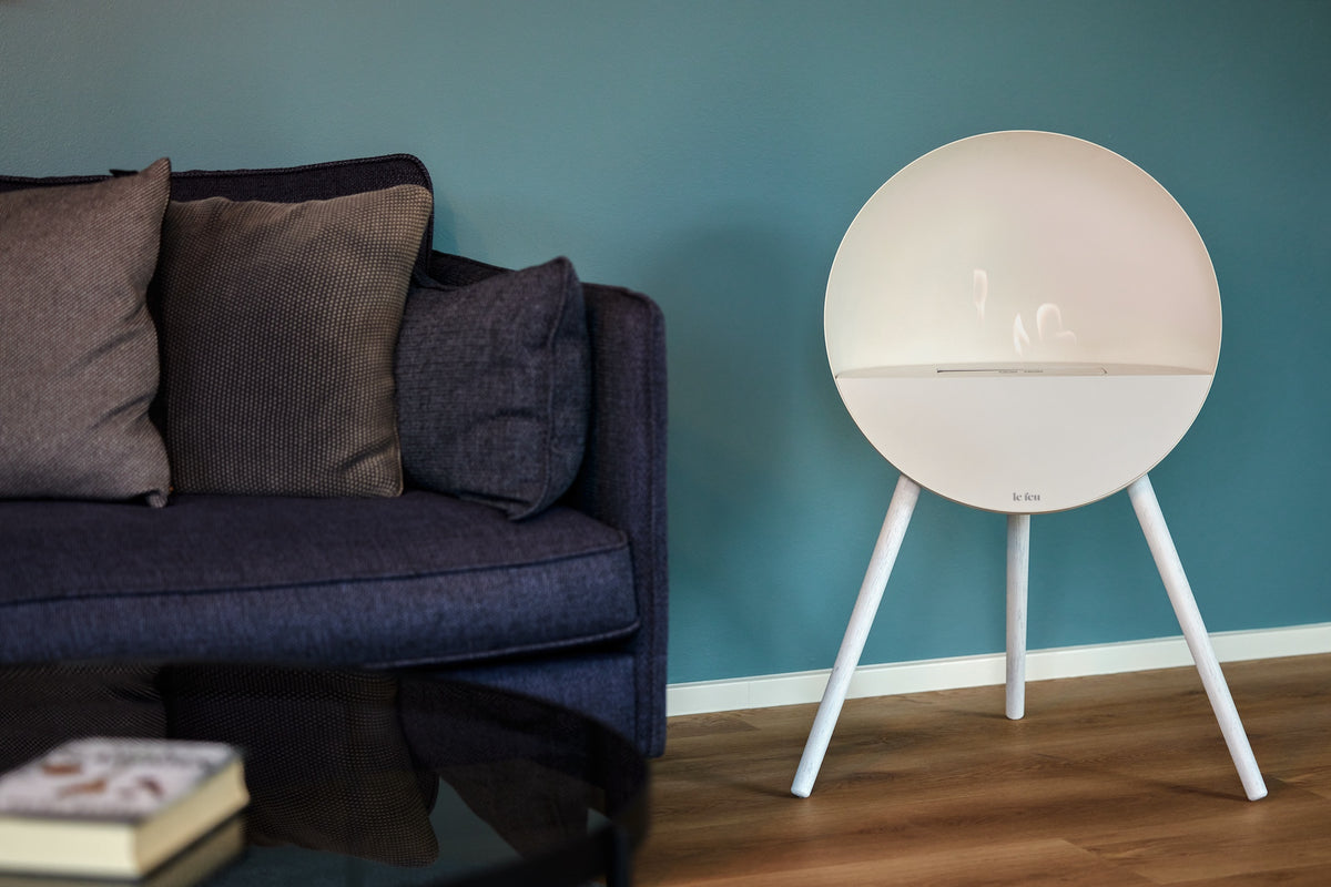 Le Feu Eye bioethanol fireplace in white with matching white oak legs creating soft Nordic warmth beside a modern sofa and teal wall