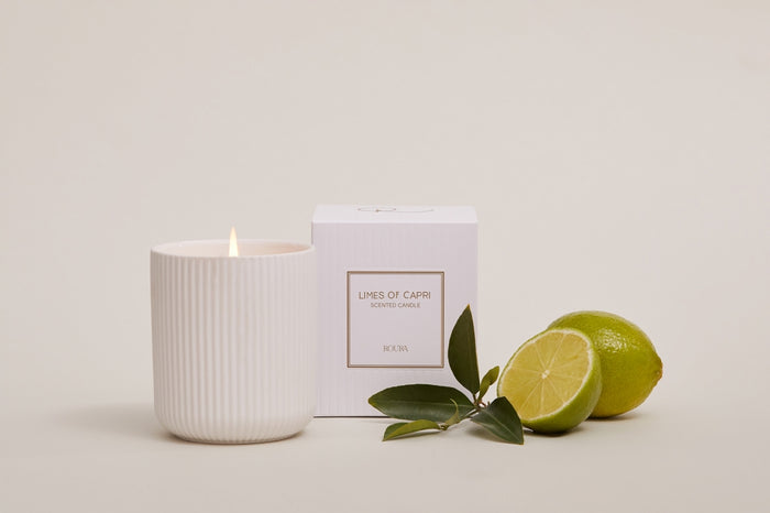 Lit Limes of Capri candle beside boxed packaging and whole and cut limes