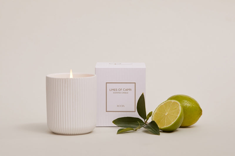 Lit Limes of Capri candle beside boxed packaging and whole and cut limes
