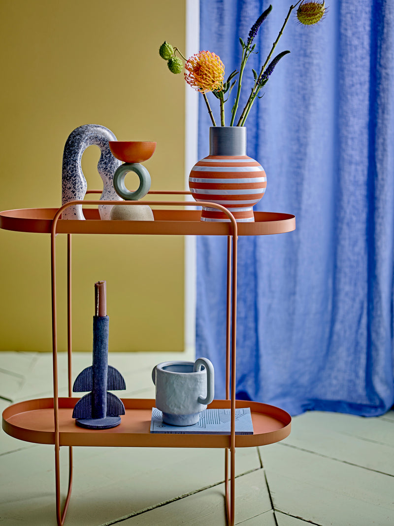 Blue and terracotta striped vase styled on orange table with colourful modern décor