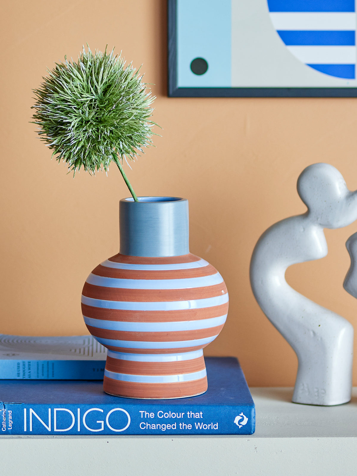 Blue and terracotta striped ceramic vase on books against peach wall