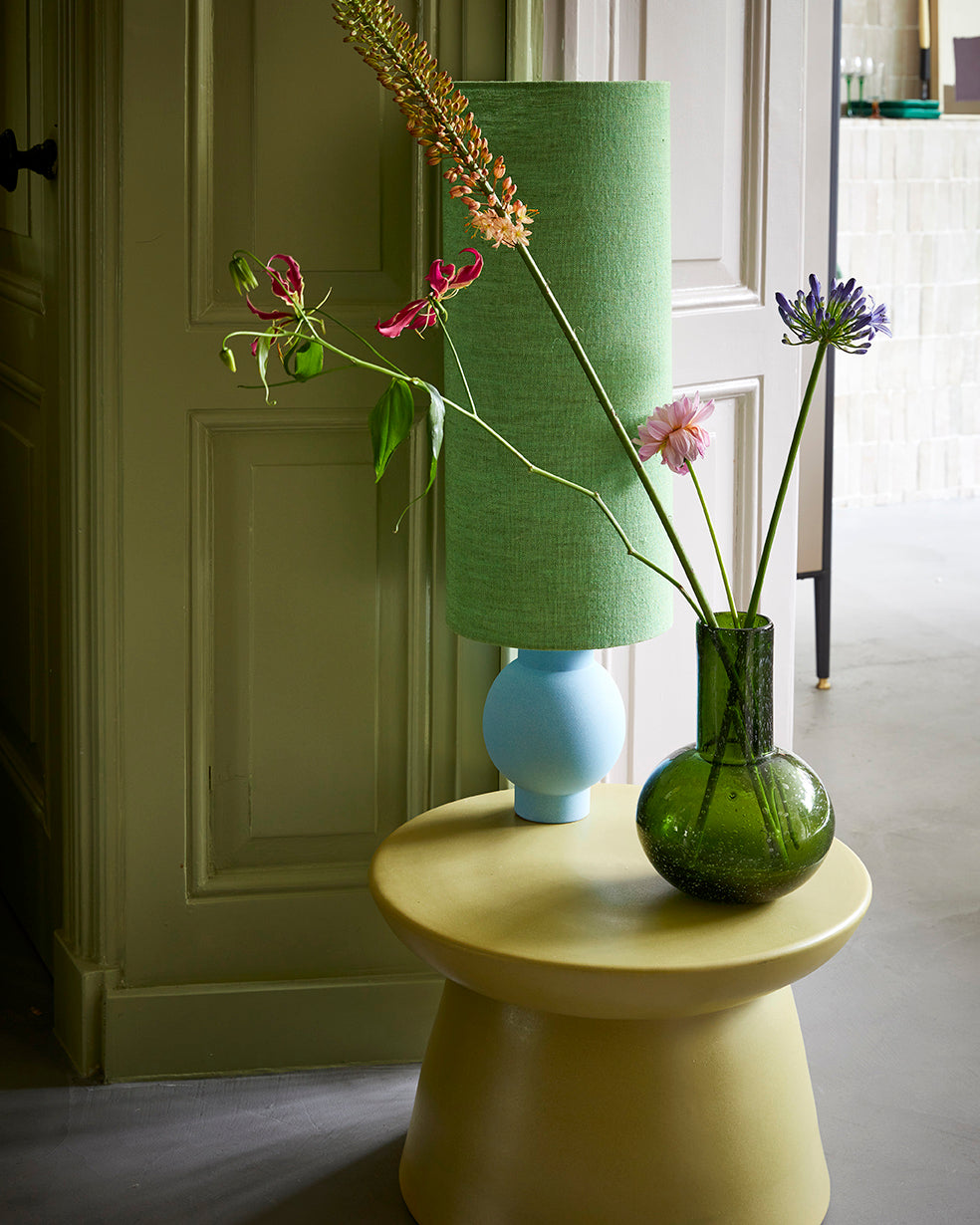 Green HKLIVING earthenware side table with a vase of flowers in front of a green panelled door