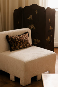 Maribel cushion by Olsson & Jensen on a cream armchair beside a painted screen