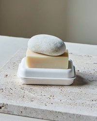 Meraki scrub stone resting on a eucalyptus soap bar in its tray on a travertine surface