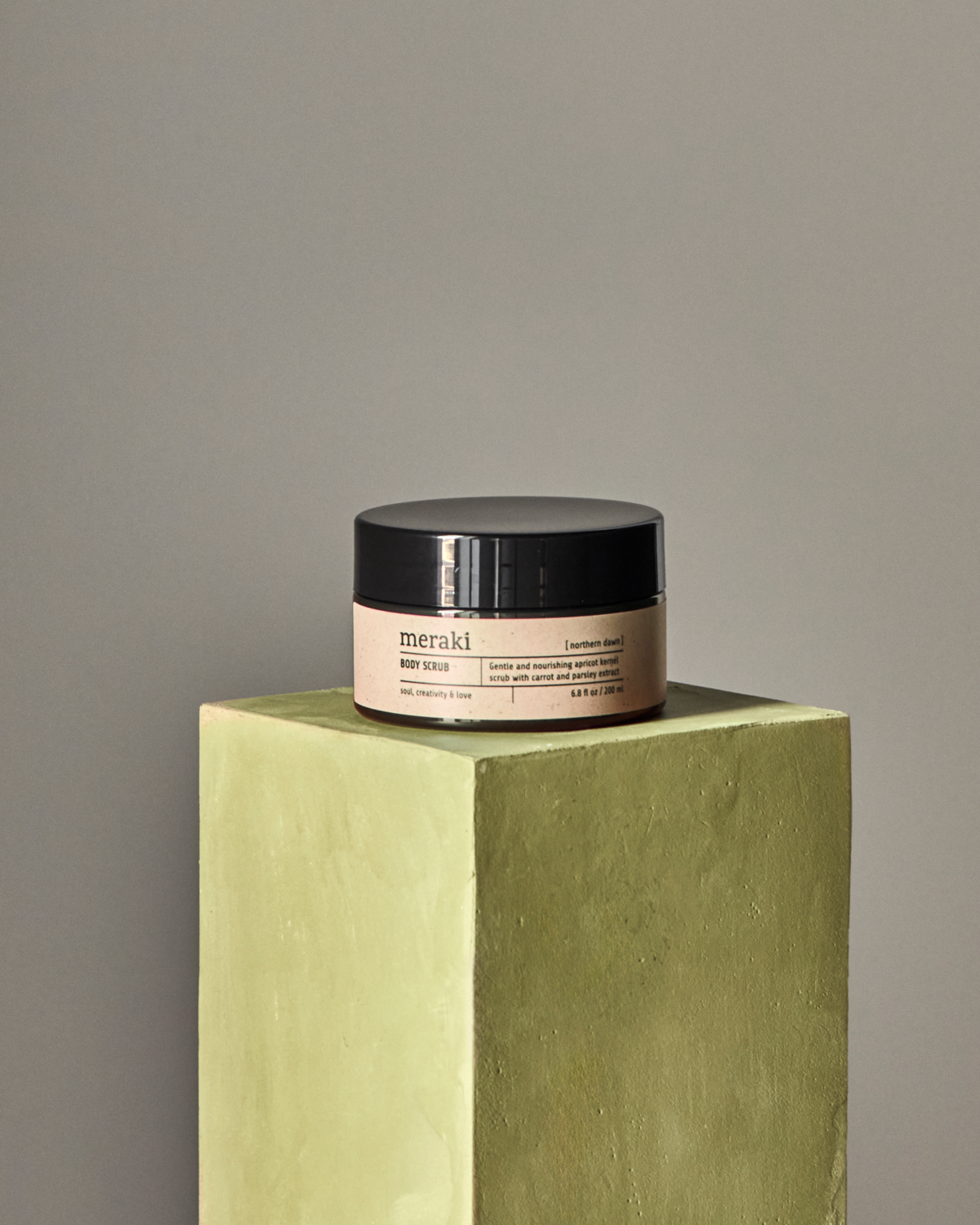 Meraki body scrub in Northern Dawn fragrance displayed on pedestal for minimalist skincare aesthetic