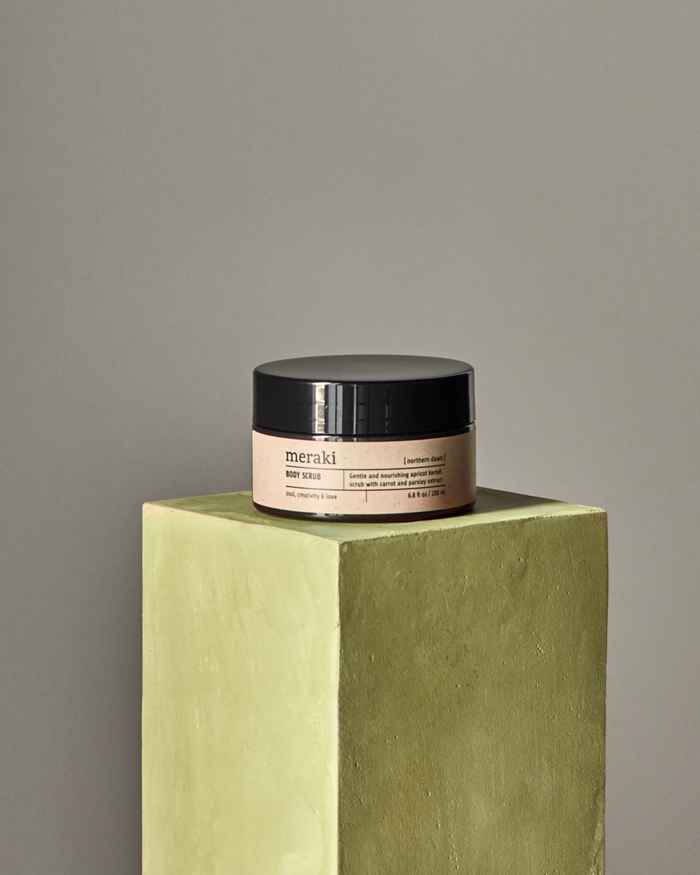 Meraki body scrub in Northern Dawn fragrance displayed on pedestal for minimalist skincare aesthetic