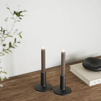 Shorter mocha LED dinner candles on a wooden surface with books and stone decor, creating relaxed evening atmosphere.
