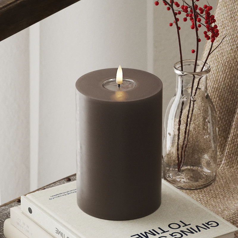 large mocha LED pillar candle glowing in a warm winter interior

