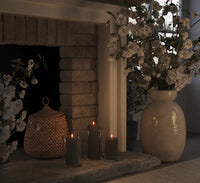 set of mocha LED pillar candles glowing warmly in glass holders on stone fireplace
