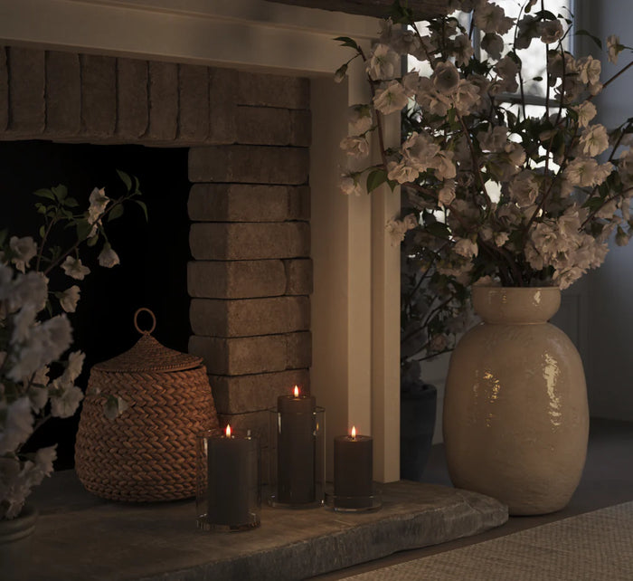 set of mocha LED pillar candles glowing warmly in glass holders on stone fireplace
