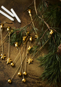 assortment of brass christmas tree candle holders with ball and star designs styled with pine branches
