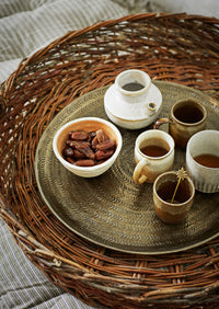 Ceramic cups and a bowl of dates on a woven tray with a woven surface background.