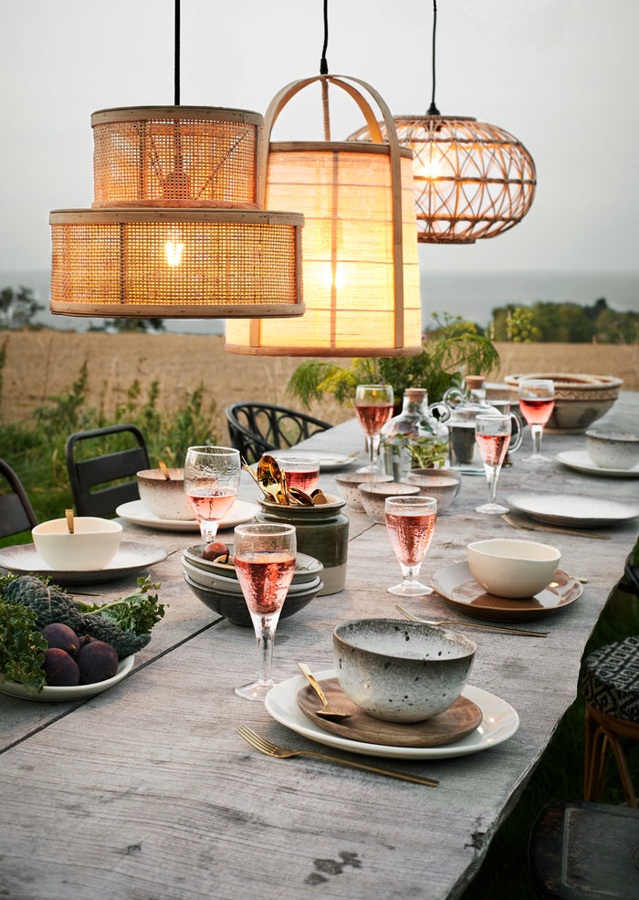 outdoor dining table styled with speckled stoneware bowls and warm lighting
