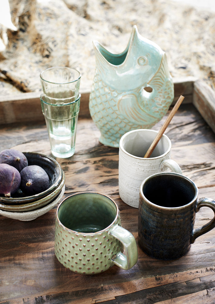 Ceramic mugs and a pitcher on a wooden surface with a natural background