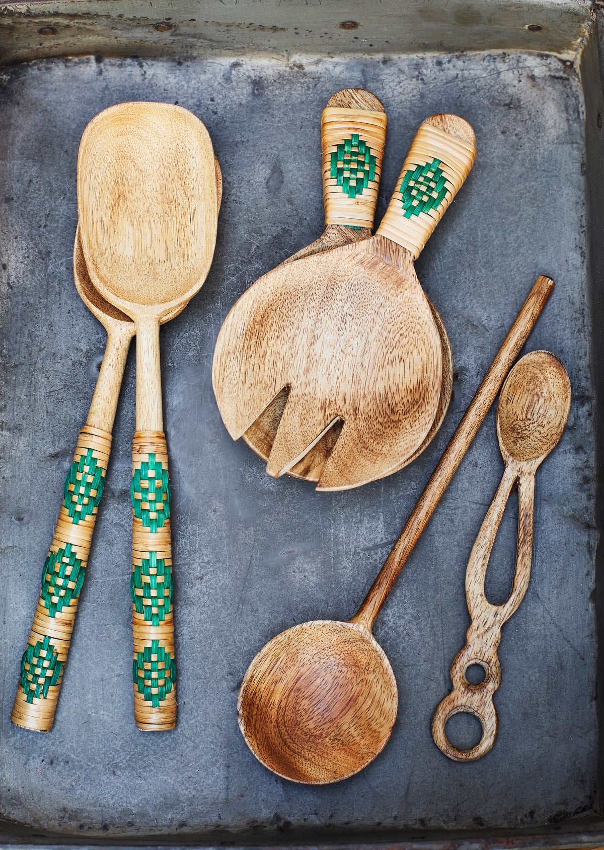 natural mango wood serving spoon styled with woven-handle utensils on grey surface