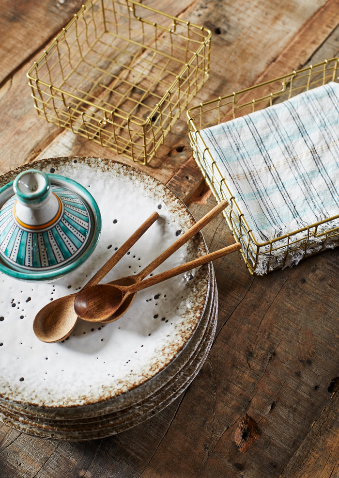 Decorative setting with wooden spoons, ceramic dish, and wire baskets on a wooden surface.