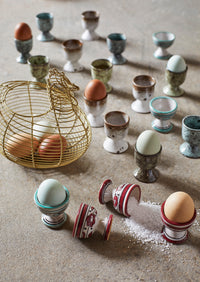 Egg cups and a wire basket with eggs on a textured surface