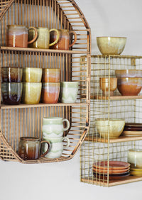 Collection of ceramic mugs and bowls on shelves with a rattan and wire frame design.