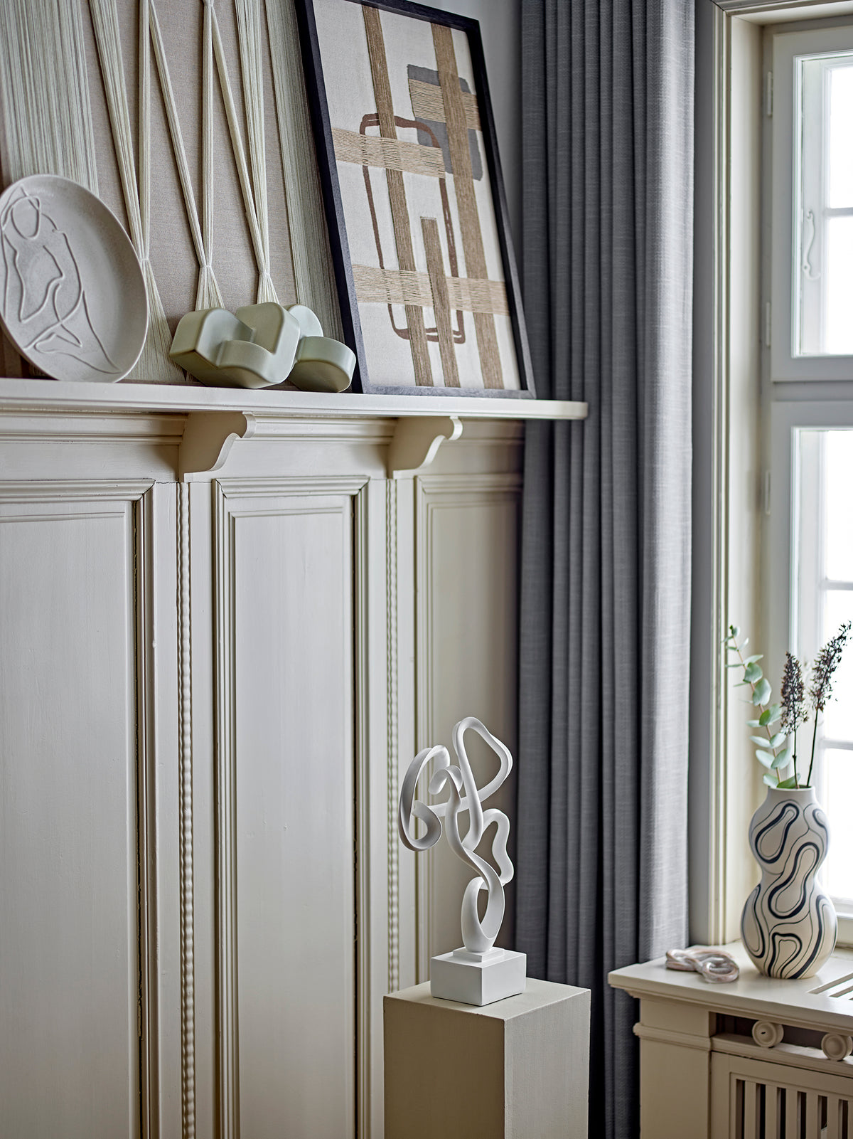 Large sculptural vase with black line pattern styled on mantel with modern artwork