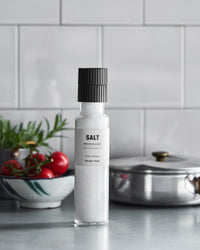 Nicolas Vahé French sea salt grinder on a kitchen worktop beside a bowl of tomatoes and a steel pan