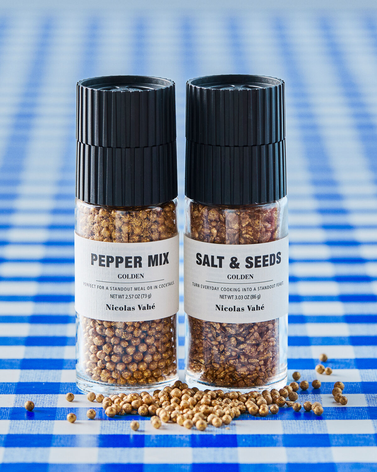 Nicolas Vahé golden pepper mix and golden salt and seeds grinders on blue gingham with scattered peppercorns