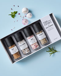Nicolas Vahé The Mixed Story salt and pepper gift box on a pale blue surface with garlic bulbs and fresh herbs