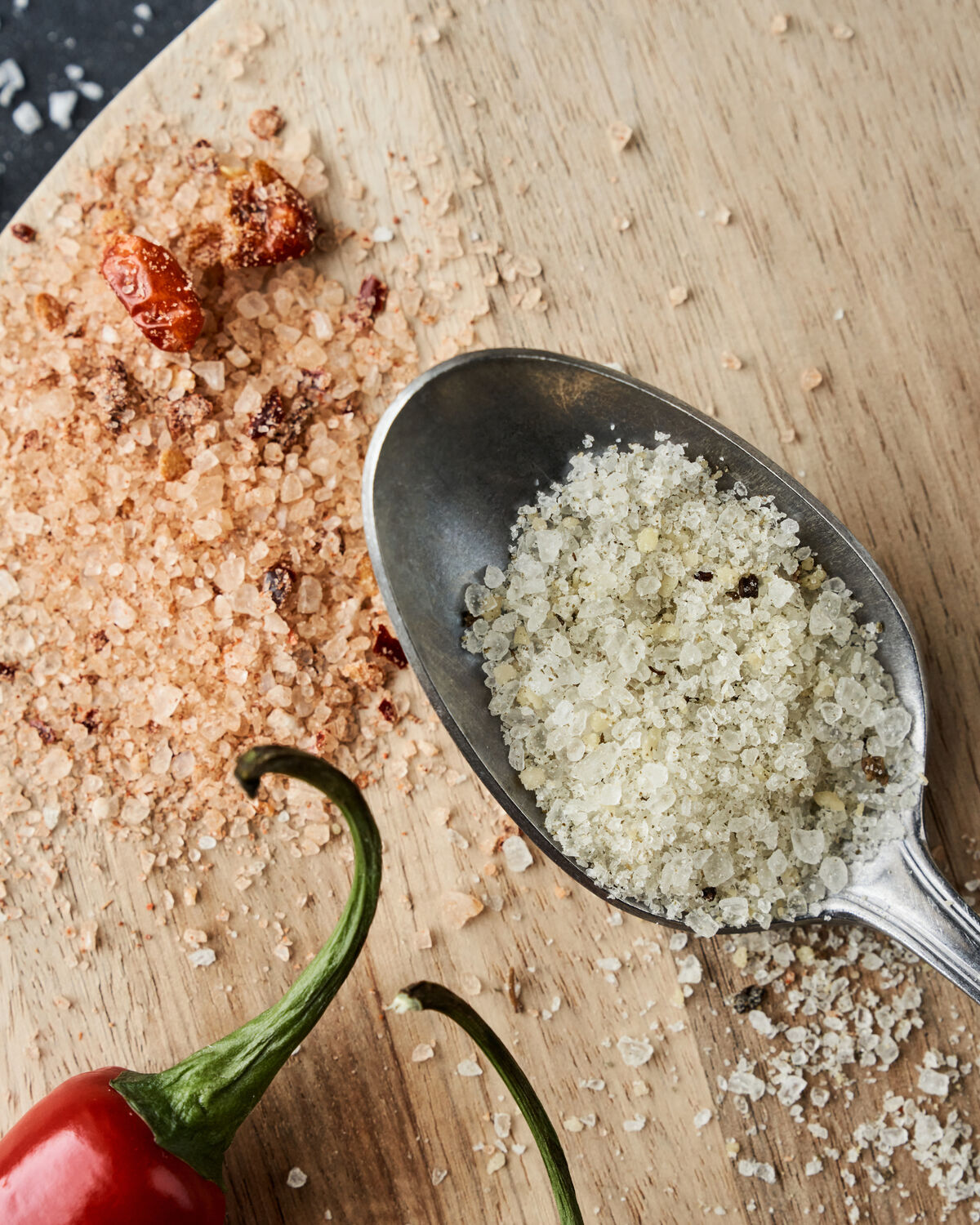 Spoonful of Nicolas Vahé Parmesan and basil salt beside chilli salt and a red chilli on a wooden board
