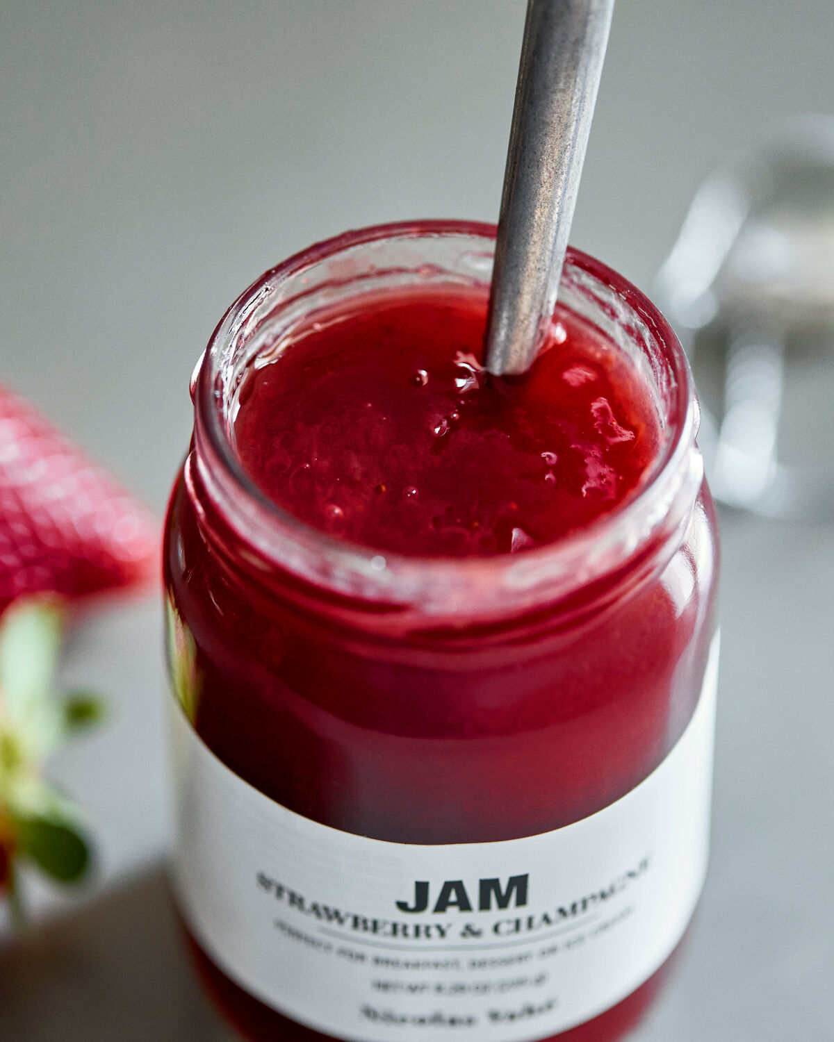 Open jar of Nicolas Vahé strawberry and champagne jam with a spoon and strawberries