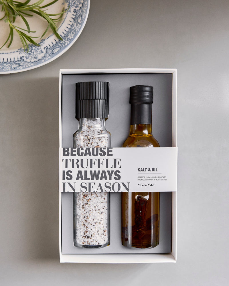 Nicolas Vahé truffle salt and oil gift box on a grey table beside a patterned plate and fresh herbs