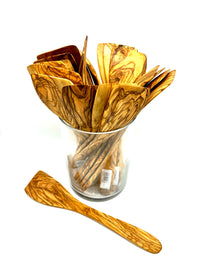 Alt text: Top view of a jar of olive wood spatulas fanned out with an extra spatula on the table