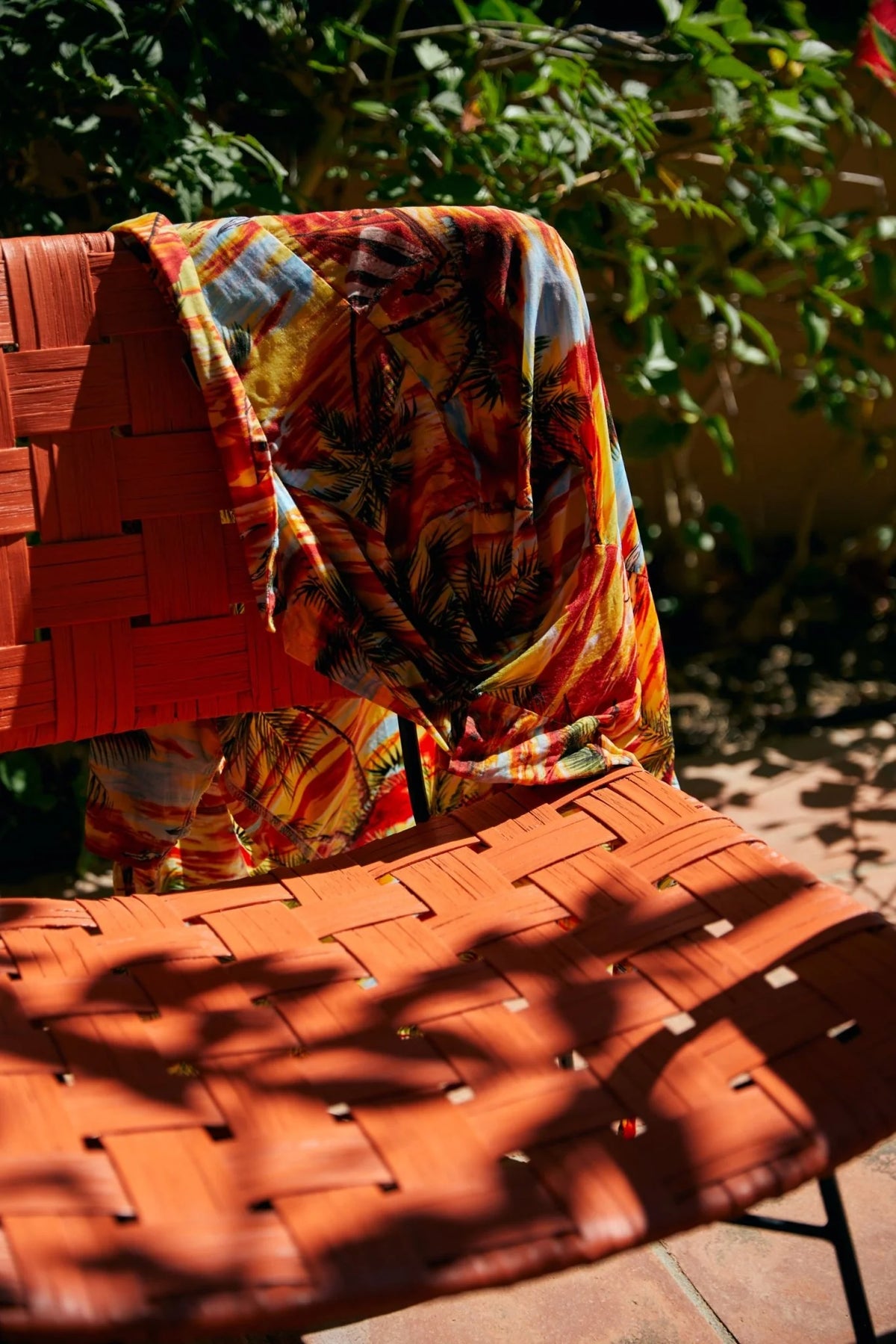 Colorful patterned fabric draped over HKLIVING woven chair with a garden background