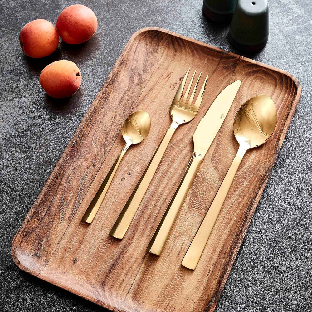 Gold cutlery set on a wooden tray with peaches and scandi salt and pepper shakers in the background