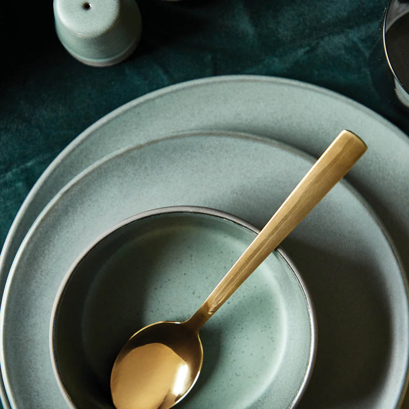 Gold Aida spoon on a stack of green ceramic plates with a dark background