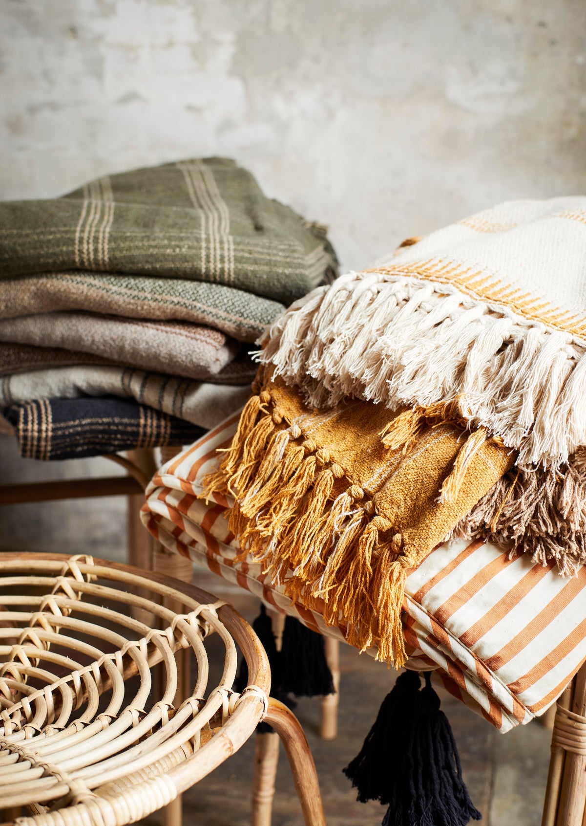 Stack of cosy textured throws in assorted earthy tones including the ecru, brown and honey recycled cotton throw
