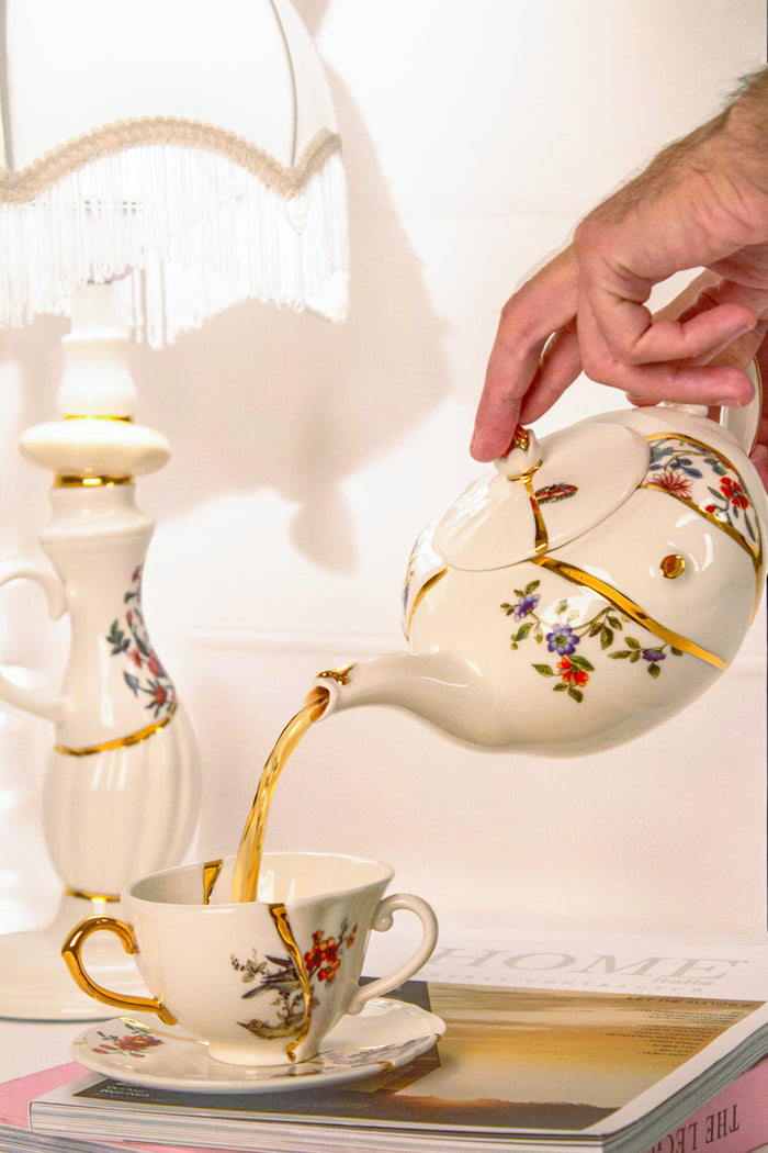 Seletti Kintsugi teapot pouring tea into matching gold-detailed cup and saucer

