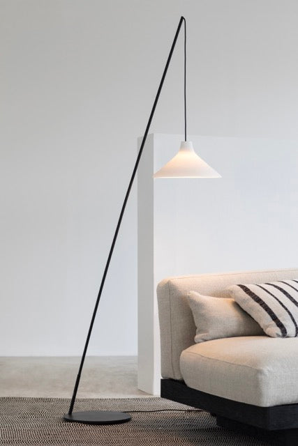 Seam porcelain floor lamp by Serax arching over a cream sofa in a minimalist living room
