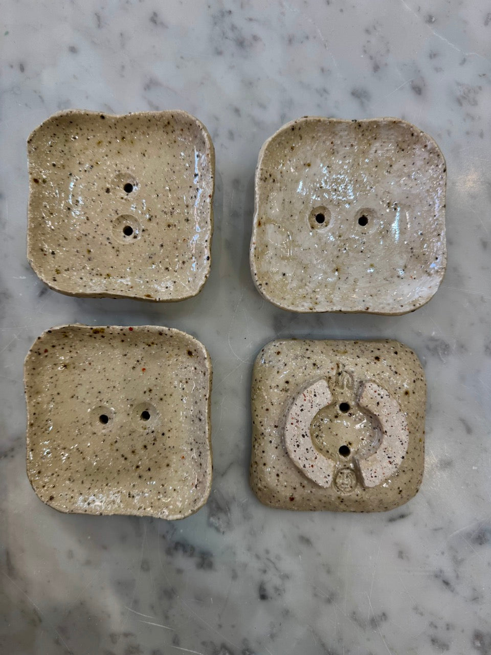 Four square ceramic soap dishes with textured surface on a marble countertop