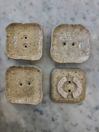 Four square ceramic soap dishes with textured surface on a marble countertop