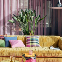 yellow couch with modern colourful tartan check in pink, purple, green, and blue with other hkliving crockery and end tables and a flourishing green plant in the background